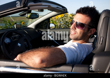 A cool man on a convertible car driving near a sunflower field Stock Photo