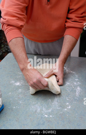 A man kneads dough on a kitchen table covered with flour. Stock Photo