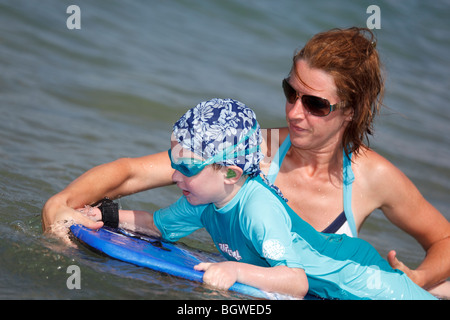 mother helps son with surfing on surfboard Stock Photo