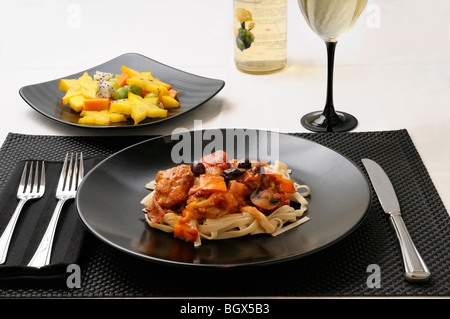 Table setting with plate of Chicken Marengo with fruit salad and white wine Stock Photo