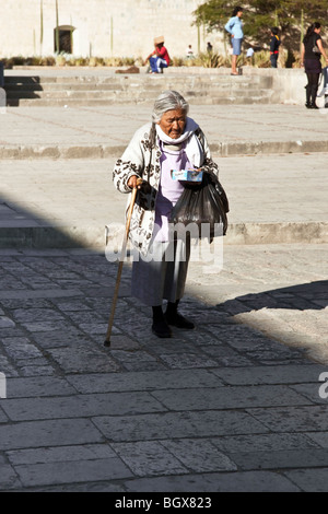 nicely dressed very old indigenous Mexican Indian woman leaning on cane crosses plaza on bright sunny day in Oaxaca City Mexico Stock Photo