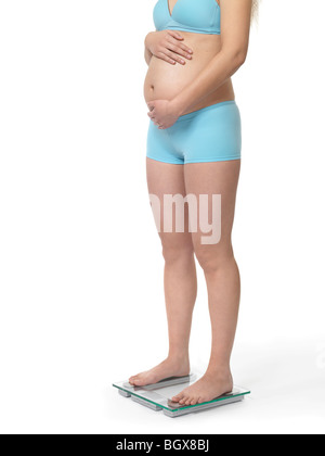 Pregnant woman standing on a weight scale. Isolated on white background. Stock Photo