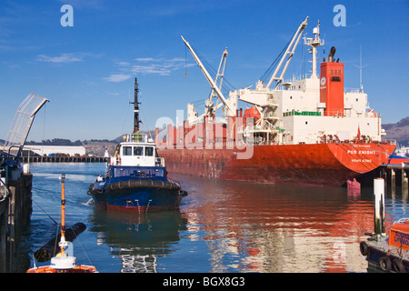 A tug approaches it's berth with a bulk carrier in the background. Stock Photo