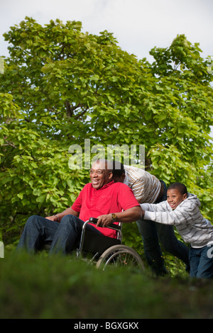 man in wheelchair pushed by children Stock Photo