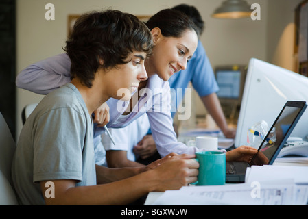 Male college student using laptop computer, female classmate looking over shoulder at laptop, smiling Stock Photo