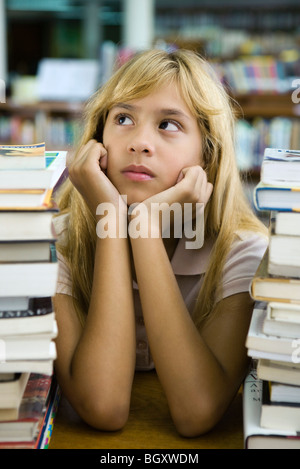 Preteen girl sitting with two large stacks of books, chin in hands, looking away Stock Photo