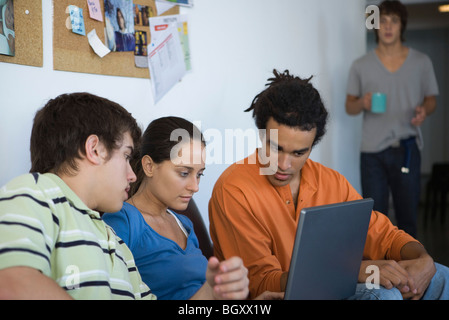 Female college student using laptop computer, friends sitting on either side watching Stock Photo
