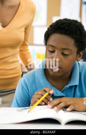 Male elementary school student reading in class while teacher observes Stock Photo