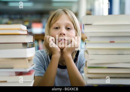 Boy leaning on elbow with look of boredom, stacks of books in foreground Stock Photo