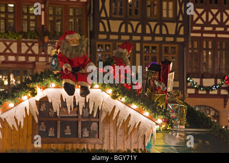 Santas Claus on the roof of a decorated Christkindlmarkt (Christmas Market) stall set up in front of buildings in the Römerberg  Stock Photo