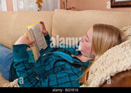 11-13 year old girl reading book on sofa at home. MR  © Myrleen Pearson Stock Photo