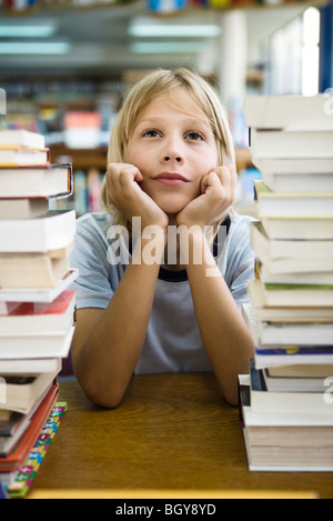 Young boy leaning on elbow daydreaming, stacks of books in foreground Stock Photo