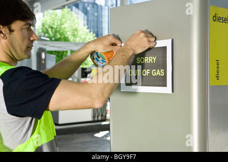 Gas station attendant posting sign at gas pump reading 'Sorry out of gas'