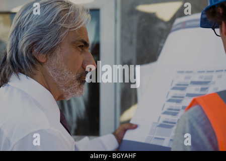 Architect and construction worker reviewing blueprint together Stock Photo