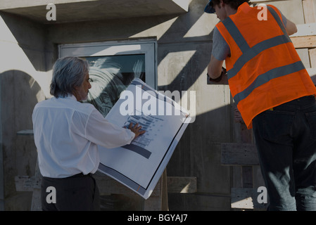 Architect showing blueprint to construction worker standing on ladder Stock Photo