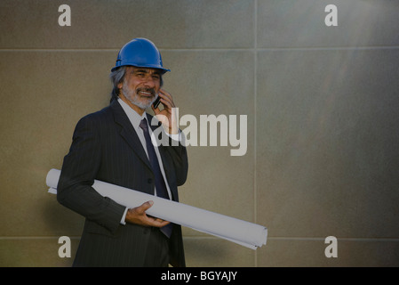 Architect talking on cell phone, carrying blueprint under arm Stock Photo