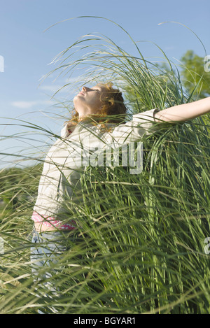 Woman standing with arms outstretched and head back in field of tall grass