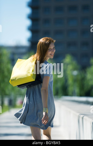 Young woman carrying shopping bags, smiling over shoulder at camera Stock Photo