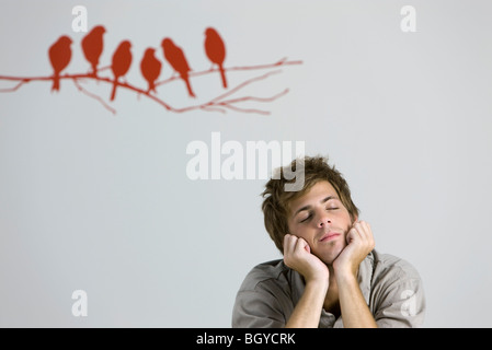 Young man resting chin on hands, smiling, eyes closed Stock Photo