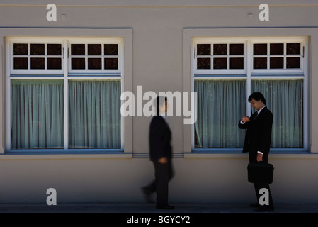 Young businessman standing on sidewalk, checking time as colleague approaches Stock Photo