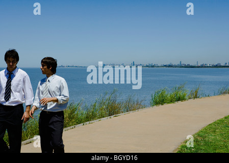 Young businessmen walking on sidewalk, talking, sea in background Stock Photo