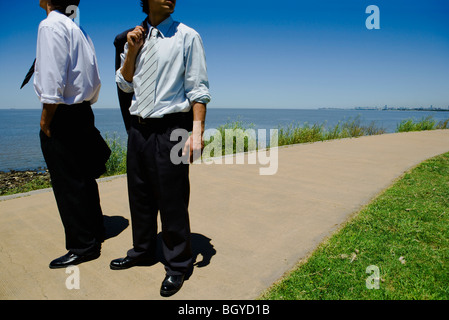 Two young businessmen standing on path, sea in background, cropped Stock Photo