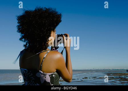 Young woman photographing coast with camera, rear view