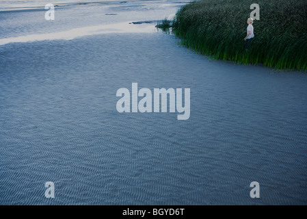 Young man standing in tall grass along coast at low tide Stock Photo