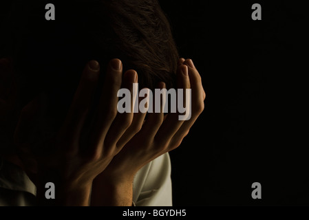 Man with head lowered covering eyes with hands Stock Photo