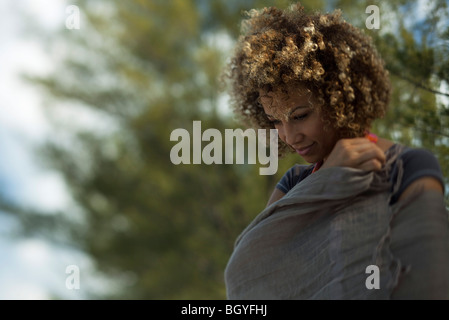 Woman outdoors, wrapped in shawl, looking down in thought Stock Photo