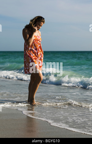 Woman walking in surf on beach, talking on cell phone Stock Photo