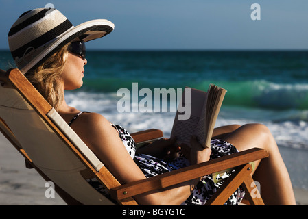 Woman relaxing in deckchair at beach, reading book Stock Photo