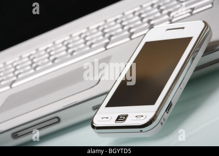 White 'touch' phone (communicator) on a high-end aluminium laptop. Shallow DOF, focus on a foreground. Modern communications. Stock Photo