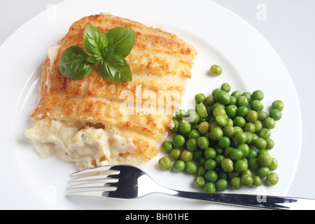 A classic fish pie made of mashed potato baked on top of bechamel sauce and cooked fish,  with green peas and basil garnish Stock Photo