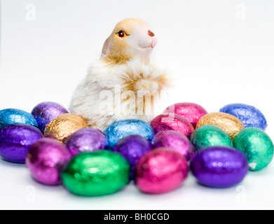 A rabbit ornament surrounded by colorful mini chocolate Easter eggs on a white background Stock Photo