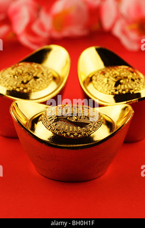 A trio of chinese gold ingots on a red background with some cherry blossoms in the background Stock Photo