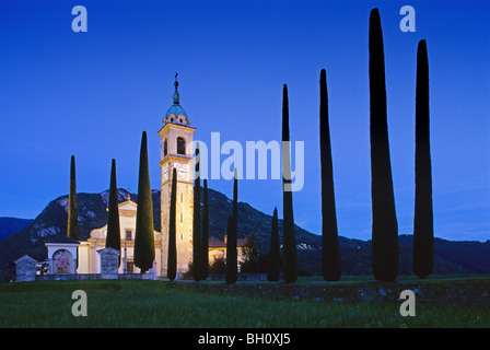 Alley with cypresses to the illuminated church Sant´Abbondio in the evening, Ticino, Switzerland, Europe Stock Photo