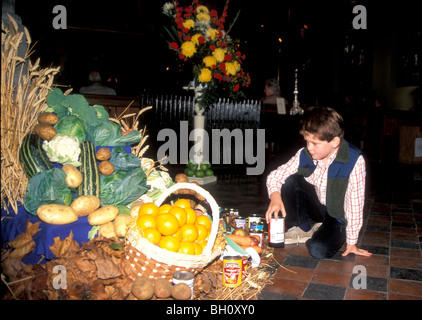 Young boy placing food for the Harvest Festival display in his church, St Saviours, Pimlico. London. Stock Photo