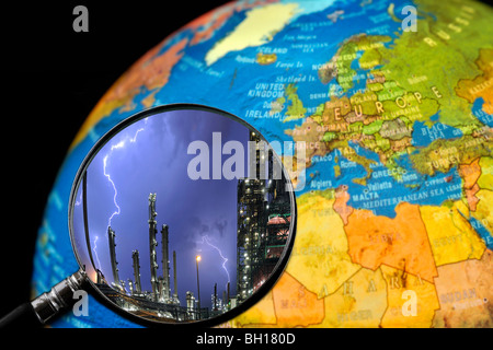 Lightning during thunderstorm above petrochemical industry seen through magnifying glass held against illuminated globe Stock Photo