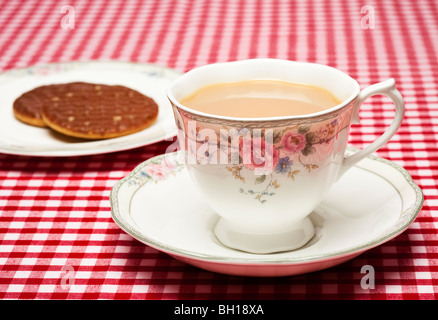 Cup of tea in a fine bone china decorated cup and saucer with a plate of biscuits on a red checked tablecloth Stock Photo
