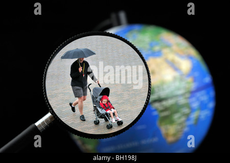 Man with umbrella pushing buggy in the rain seen through magnifying glass held against illuminated terrestrial globe Stock Photo