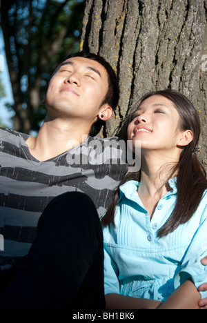 Young couple seated at base of tree, faces lifted upwards, Assiniboine Park, Winnipeg, Manitoba, Canada Stock Photo
