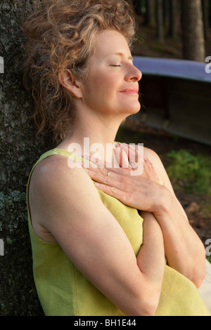 Woman leans against tree with hands folded over chest, Clear Lake, Manitoba Stock Photo