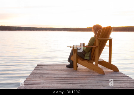 Woman seated in deck chair on dock at sunset, Clear Lake, Manitoba Stock Photo