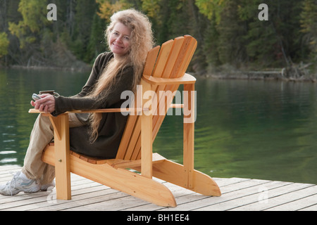 Smiling woman seated in deck chair on dock, Clear Lake, Manitoba, Canada Stock Photo