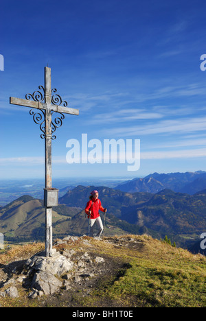 Woman reaching summit cross, Kleiner Traithen, Bavarian foothills, Bavaria, Germany Stock Photo