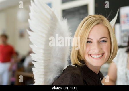 Mid adult woman wearing angel wings sitting in a cafe Stock Photo