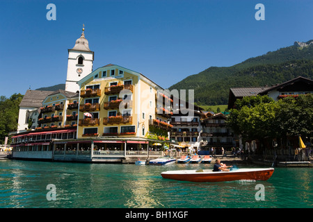 View over lake Wolfgangsee to parish and pilgrimage church and Hotel Im Weissen Roessel am Wolfgangsee, two people in a canoe pa Stock Photo
