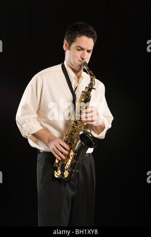 Mid adult man stands in shirt playing the saxophone Stock Photo