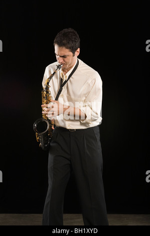 Mid adult man stands in shirt playing the saxophone Stock Photo